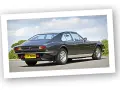 Klasyczny Aston Martin Lagonda w ciemnym kolorze, widziany z tyłu, na tle błękitnego nieba z chmurami.