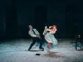 Dramatyczna scena z opery lub operetki: mężczyzna w garniturze i kobieta w zwiewnej sukni krzyczą, wyginając ciała w ekspresyjnych pozach.