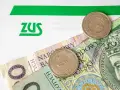 ZUS i polskie złotówki. Kiedy będzie 300 plus? Pieniądze i monety na tle dokumentu ZUS.