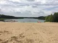 Piaskowa plaża nad jeziorem, z pomostami i łódkami. W oddali las, chmury na niebie. Idealne miejsce na wypoczynek nad wodą.