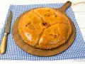 Empanada dorada y decorada sobre tabla de madera, con cuchillo y mantel a cuadros.