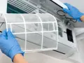 Mani guantate rimuovono il filtro del condizionatore per pulirlo. Un passo essenziale per un'aria fresca e pulita.