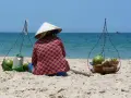 Sprzedawczyni kokosów na plaży w Mui Ne, Wietnam. W tle błękitne morze i niebo.