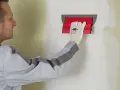 Un ouvrier utilise un outil pour appliquer une bande de placo sur un mur.