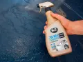 Dłoń trzyma butelkę z woskiem w sprayu K2 SPID WAX, gotową do usunięcia dziwnych plam na lakierze samochodowym.