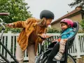 En kvinna med hjälm ler mot ett litet barn i en cykelbarnstol. De är redo att cykla med bebis i det vackra vädret.