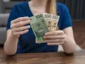 Dłonie trzymają polskie banknoty: 100 zł i dwa razy po 200 zł. To może być część zasiłku rodzicielskiego.