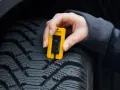 Misurazione del battistrada di uno pneumatico con un calibro giallo. La **sigla TWI** indica il limite di usura.
