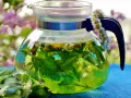 Thé vert infusé avec des fleurs de marguerite et de la menthe dans une théière en verre. Une guirlande de marguerites décore la anse. Une belle illustration de la différence entre décoction et infusion.