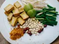 Składniki do pad ka prow: smażone kostki tofu, kiełki fasoli mung, szczypiorek, orzeszki ziemne, limonka i płatki chili.