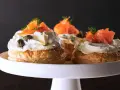 Wykwintne ciasto francuskie z łososiem i serkiem Almette, ozdobione kaparami i koperkiem. Idealna przekąska na eleganckie przyjęcie.