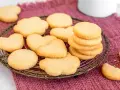 Deliziosi dolci da fare in casa, biscotti a forma di cuore e fiori su un vassoio di metallo, adagiati su un panno color prugna.