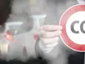 Dłoń trzyma znak zakazu z napisem CO2 na tle dymiących samochodów w korku.