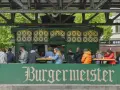 Menschen sitzen an Tischen vor dem Burgermeister in Berlin.