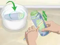 Brosse pour nettoyer peinture acrylique sèche sur une bouteille. Une autre bouteille trempe dans un bol d'eau.