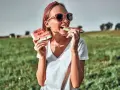 Dziewczyna w okularach zajada soczyste kawałki arbuza na tle zielonego pola. To idealny moment, kiedy jest sezon na arbuzy!