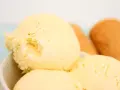 Cremoso helado de vainilla con motas oscuras, servido en un tazón blanco. Al fondo, conos de helado dorados esperan.