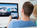 Ein Paar verbindet sein iPad mit dem Fernseher, um die Berglandschaft auf dem großen Bildschirm zu genießen.