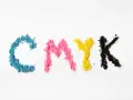 Litery CMYK ułożone z kolorowego proszku. Kolejność kolorów: cyjan, magenta, żółty, czarny.
