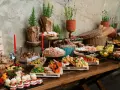 Stół z bogatym cateringiem: sery, wędliny, owoce, słodkości i pieczywo.