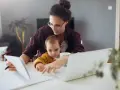 Mama z dzieckiem przy biurku, pracująca zdalnie. Kosiniakowe dla kogo? Dla rodziców łączących pracę z opieką nad dzieckiem.