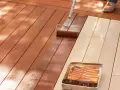 Aplicando protector para proteger madera exterior. Un rodillo extiende el líquido sobre las tablas de madera de una terraza.