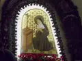 Obraz przedstawia św. Teresę z Ávili podczas modlitwy, symbolizującą nowenna do św. Rity. W tle złote róże, a u dołu czerwone kwiaty.