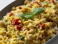 Un piatto colorato con la ricetta cous cous: chicchi dorati, pomodorini, mais e ceci, guarnito con foglie di basilico fresco.