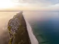 Widok z lotu ptaka na malownicze chałupy nad morzem, z piaszczystą plażą i spokojną wodą.