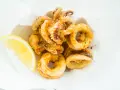 Crujientes calamares a la andaluza, dorados y sazonados, servidos con una rodaja de limón fresco.
