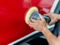 Ręce polerują czerwony lakier auta maszyną polerską. To kluczowy etap, jak woskować auto, by uzyskać lustrzany połysk i ochronę.