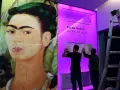 Un portrait de Frida Kahlo, avec deux hommes installant une affiche pour une exposition sur son histoire.