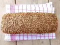 Ein rustikales Brot, bedeckt mit vielen Sonnenblumenkernen, liegt auf einem karierten Küchentuch.