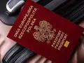 Czerwony paszport Polski z godłem orła leży na brązowej walizce.