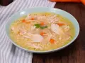 Un confortevole brodo di pollo con pezzi di pollo sfilacciato, carote e un rametto di prezzemolo, servito in una ciotola azzurra.