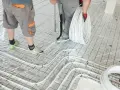 Pracownicy układają rury do ogrzewania podłogowego na siatce. Wkrótce powstanie tu szlichta, która zapewni komfort cieplny.