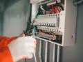 Elektryk w białych rękawicach pracuje przy skrzynce z bezpiecznikami, próbując ustalić, dlaczego wybija główny bezpiecznik.