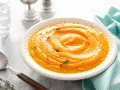 Un bol de velouté de purée de butternut, garni de thym frais, prêt à être dégusté avec une cuillère en argent.
