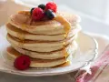Pancakes senza uova dorati, impilati e inzuppati di sciroppo, guarniti con lamponi e mirtilli freschi.