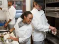 La brigada de cocina y sus funciones: chefs preparan alimentos, uno corta vegetales, otro cocina en sartén y otro lava utensilios.