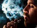 Hombre vapeando, el vaper sin nicotina es malo. El humo azul forma figuras fantasmagóricas.