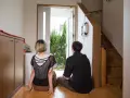 Para siedzi na podłodze w sieni, patrząc na otwarte drzwi. Widok na zielone drzewa.