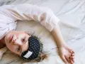 Kobieta w piżamie leży na łóżku z opaską na oczy. Z pewnością czeka ją błogi **zolpic**.