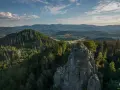 Widok na skalne formacje Rudawy Janowickie, porośnięte lasem, z ludźmi na szczycie. W tle rozległa panorama gór i dolin.