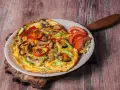 Pyszny omlet z pieczarkami, papryką i cukinią, udekorowany pomidorem i sałatą.