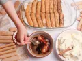 Dziecko zanurza biszkopty w kawie, przygotowując warstwy do tiramisu. Obok krem i kakao.