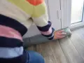Ocieplanie drzwi wejściowych: osoba w kolorowym swetrze układa podkładkę izolacyjną pod drzwiami, by zatrzymać przeciągi.