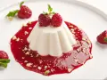 Panna Cotta przepis: kremowy deser z malinami, pistacjami i miętą na białym talerzu.