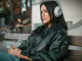 Młoda kobieta w słuchawkach, słuchająca podcastu o wymowie francuskiej, siedzi na ławce, trzymając telefon.