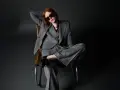 Donna con outfit giacca doppiopetto donna a righe grigie, occhiali da sole, seduta su una poltrona di pelle.